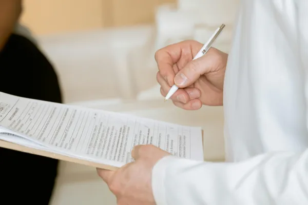 Close-up of a person holding a pen and filling out a referral form